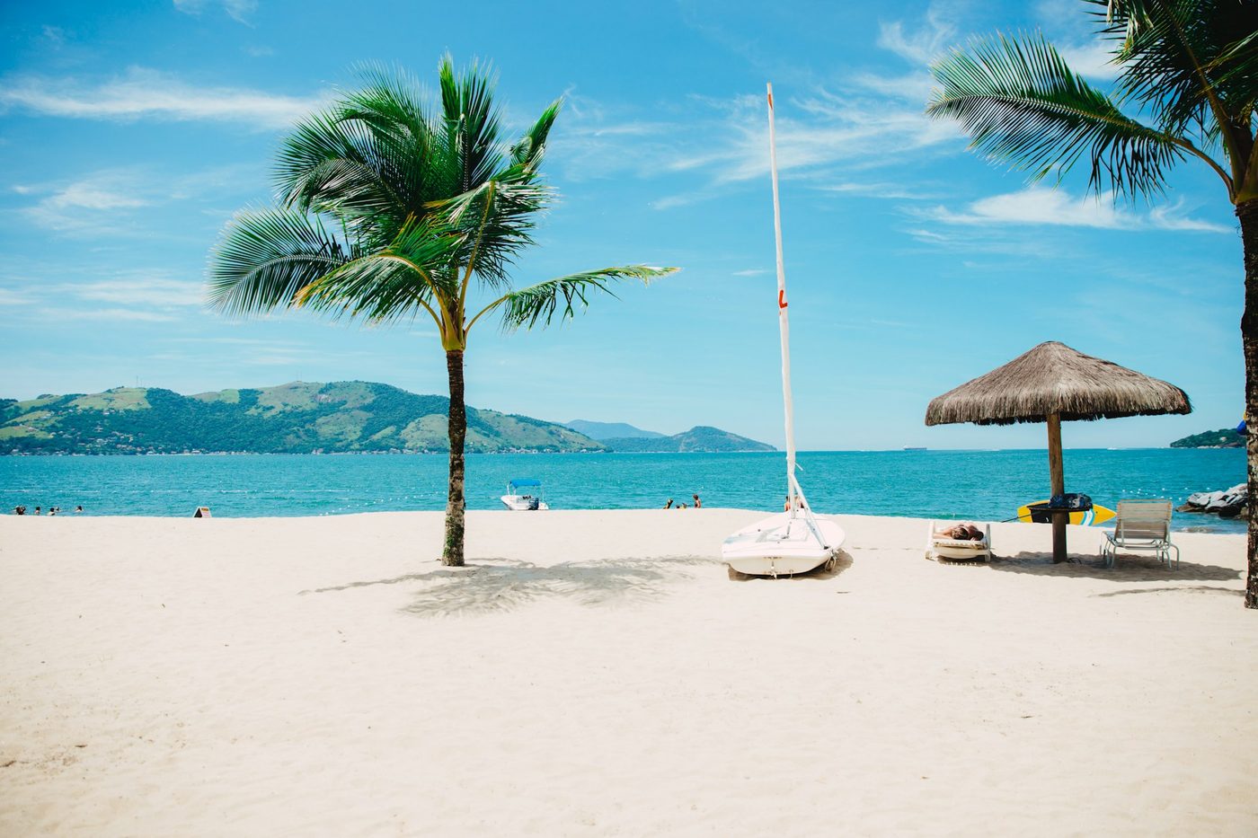 Playa con palmeras, un velero varado en la arena y montañas al fondo